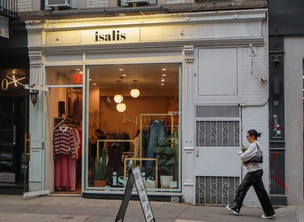 A woman walks by a white storefront with black text above the door that reads “isalis.”