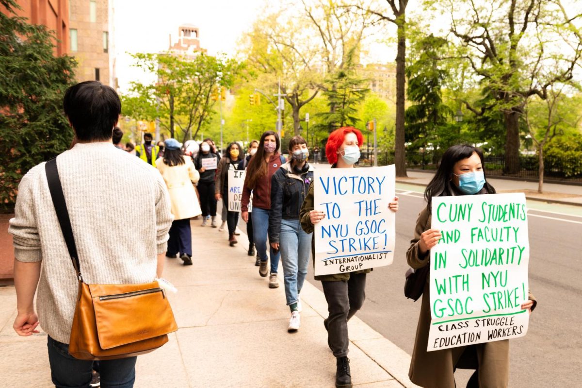 A group of people in masks hold up various signs that say “VICTORY TO THE N.Y.U. G.S.O.C. STRIKE! INTERNATIONALIST GROUP” and “C.U.N.Y. STUDENTS AND FACULTY IN SOLIDARITY WITH N.Y.U. G.S.O.C STRIKE! CLASS STRUGGLE EDUCATION WORKERS.”