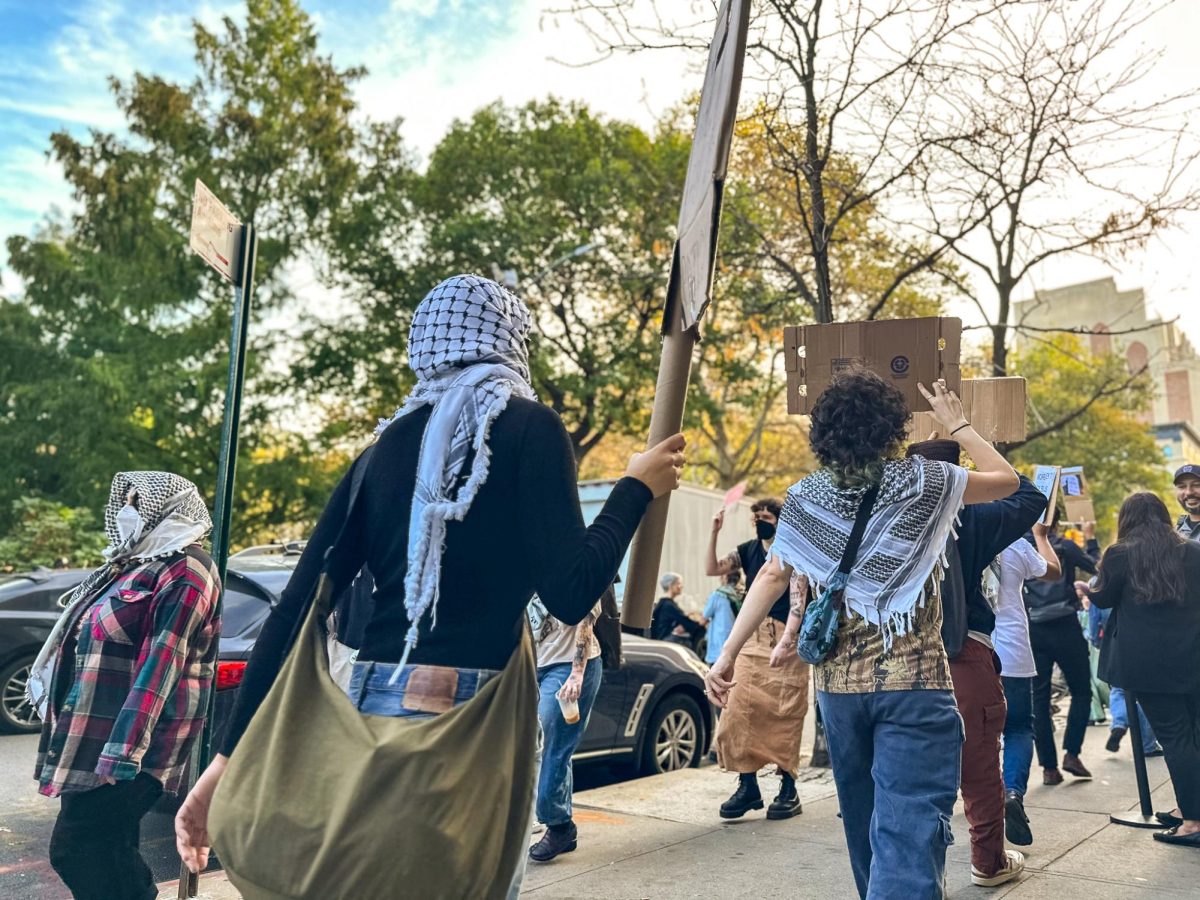 Protesters wearing keffiyehs hold signs and march on a sidewalk.