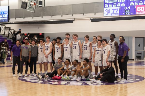 The N.Y.U men’s basketball team and coaches pose for a photo on the court.