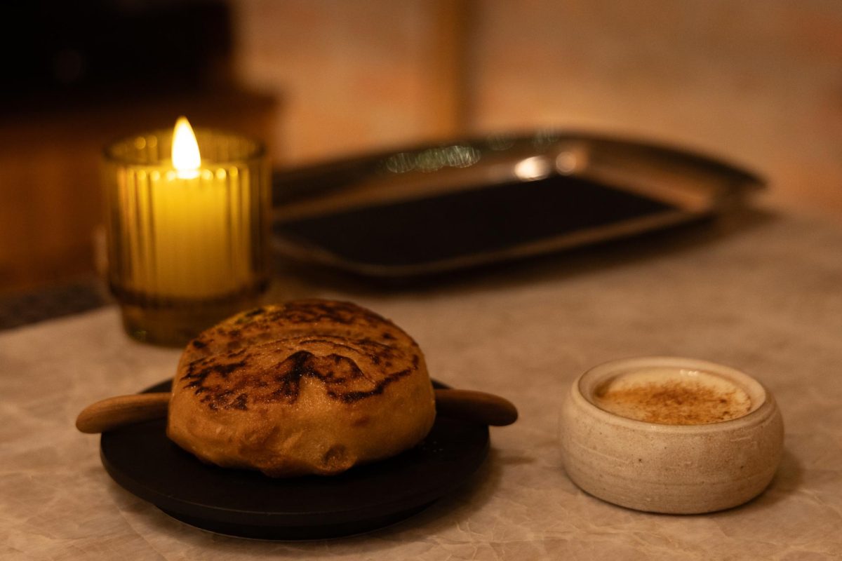 A bread circle on a black plate with a white cream sauce in a small, white bowl.