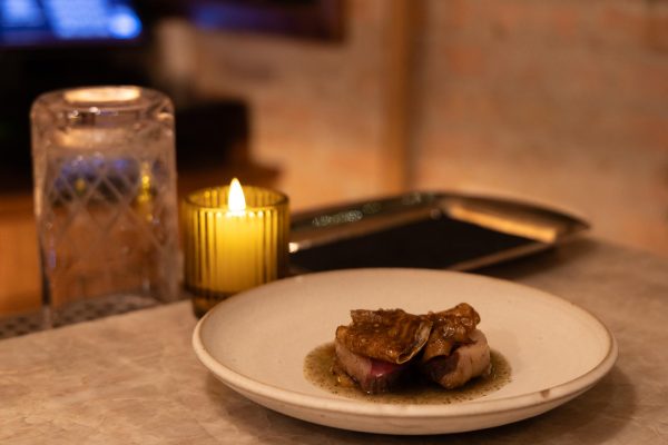 Two pieces of meat with celery root on top of it, on a white plate.