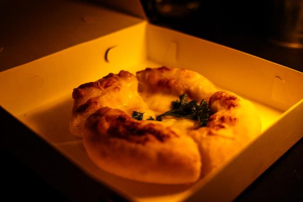 A puffy cheese pizza with a dark green leaf on top of it, in a small, cardboard box.