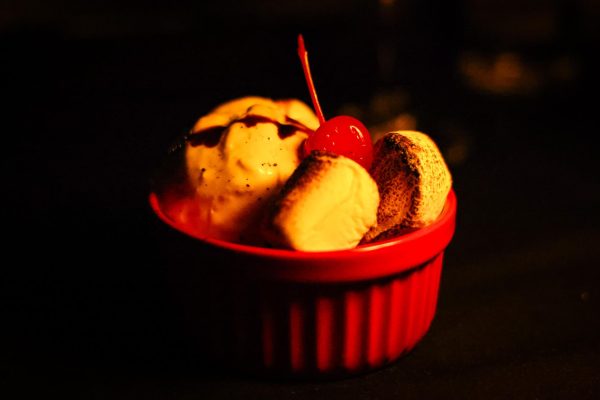 Vanilla ice cream with a chocolate drizzle on top, toasted marshmallows and a maraschino cherry on top, all in a red bowl.