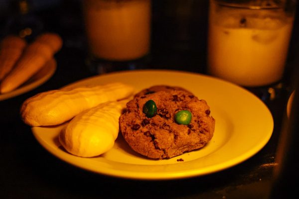 A plate with an M&M cookie and two carrot meringues on its left. Two candles are behind the plate.