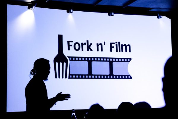 A screen with the words “Fork n’ Film” projected onto it, with an image of a fork and a film reel below it.