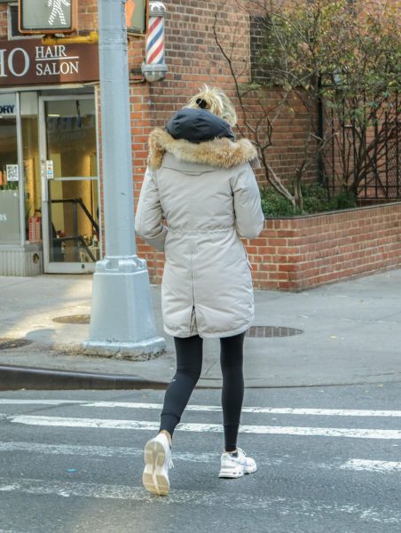 A woman in a puffer jacket and leggings walking on the street.