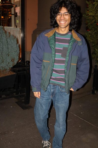 A man smiling, wearing a jacket, jeans and a striped shirt.