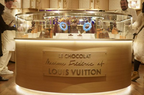 A display table with several decorative chocolates. Words on the front of the table read “LE CHOCOLAT, Maxime Frédéric at Louis Vuitton.”