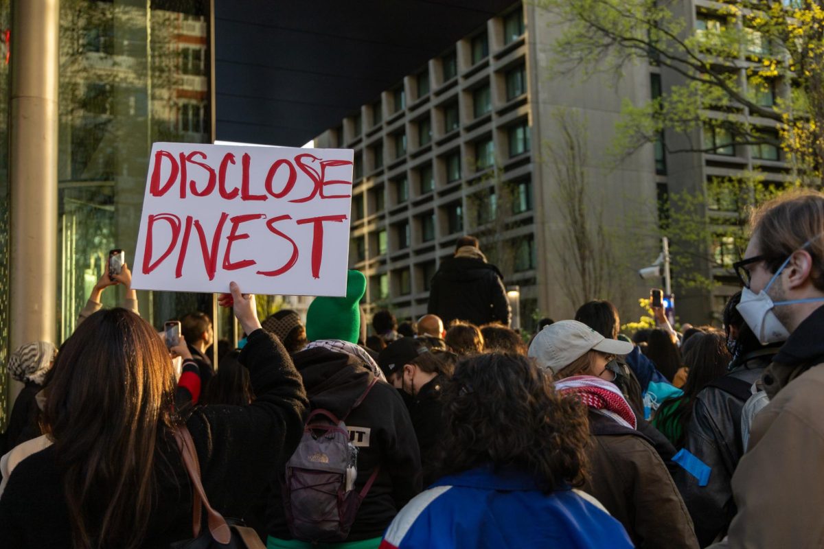 A protester holds up a white sign that reads “DISCLOSE, DIVEST”.