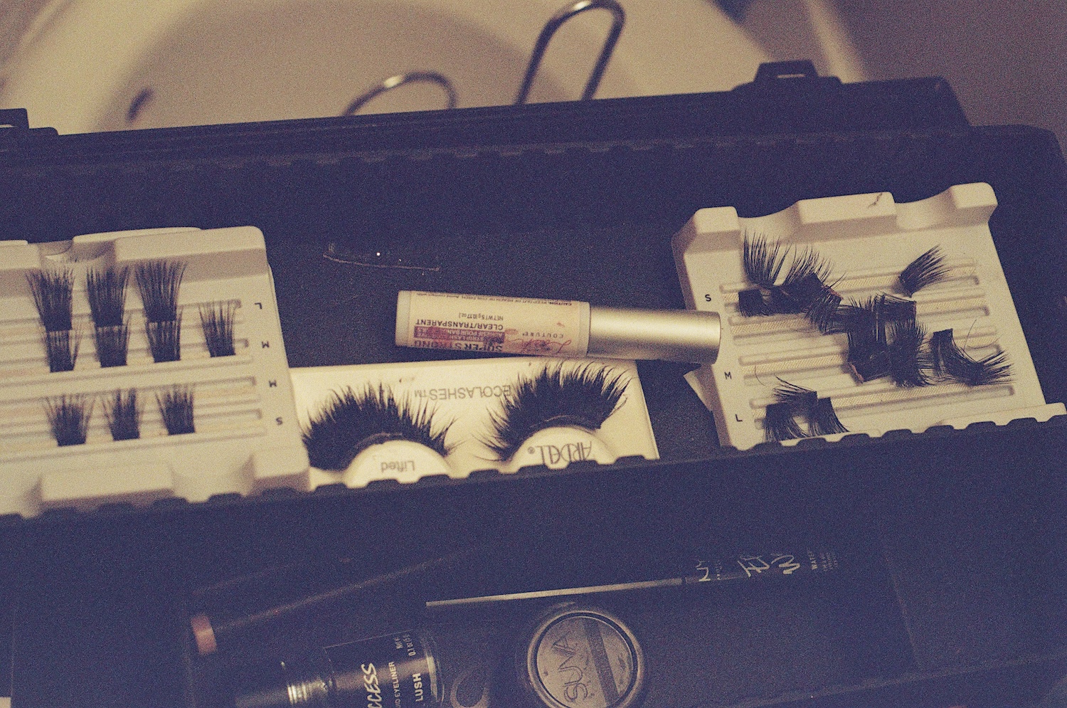 An assortment of eyelashes, lash glue and other makeup items in a black case.