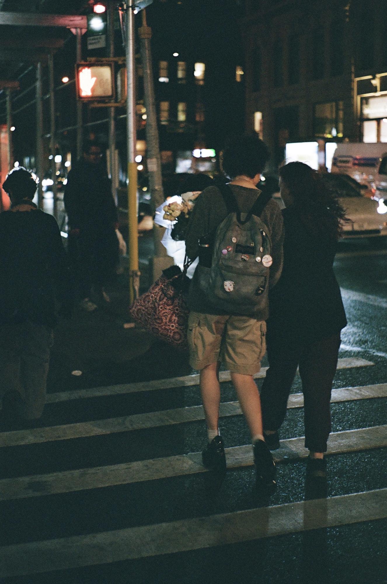 Two people walk across a crosswalk at night.