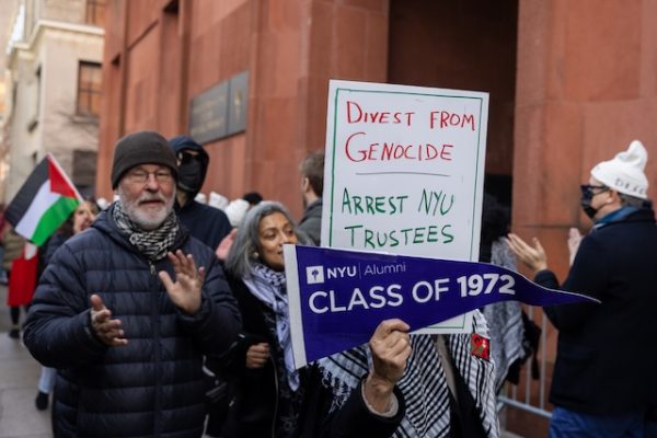 People picket in front of a red building with signs reading "DIVEST FROM GENOCIDE," "ARREST NYU TRUSTEES" and "CLASS OF 1972."