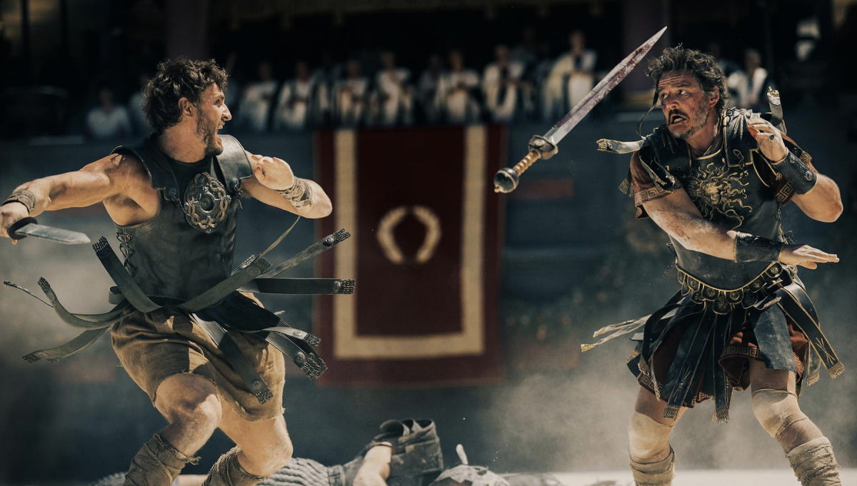 A sword hangs in mid-air between two men fighting in black and gold gladiator armor. Spectators watch from raised seats behind them.