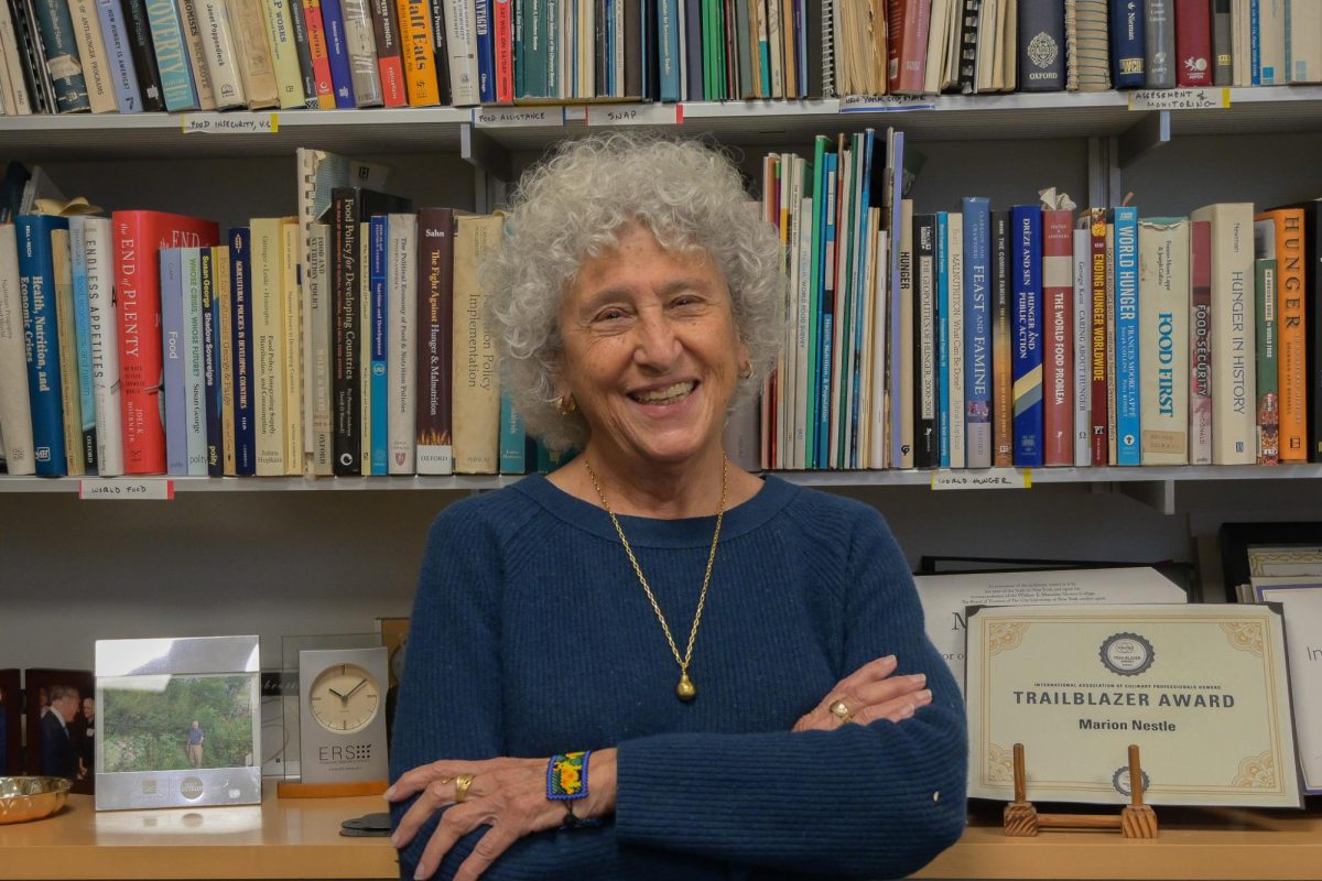 A woman wearing a blue sweater smiles while standing in front of a bookshelf.