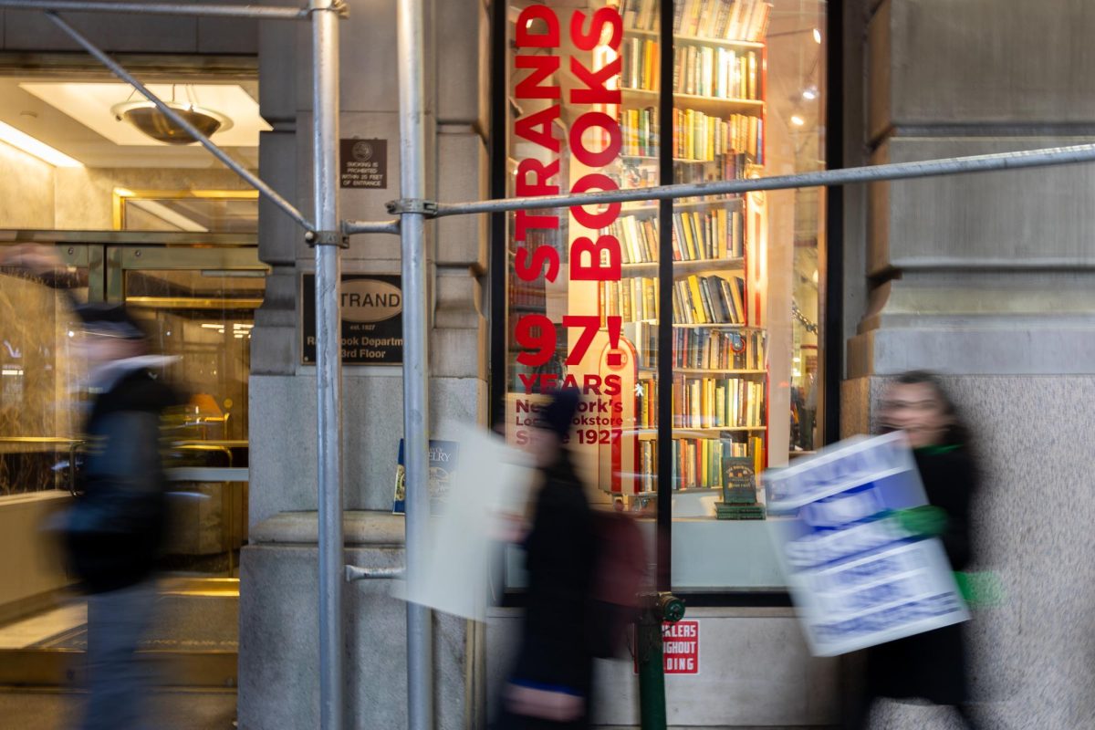 People walking outside of a building that reads “STRAND BOOKS” while holding signs.