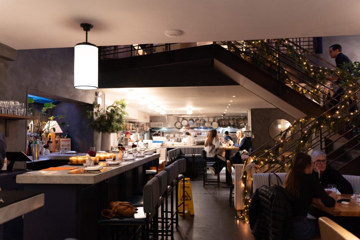 The interior of a restaurant with several tables and bar seating. A staircase leading up to a second level is lined with garlands and holiday lights.