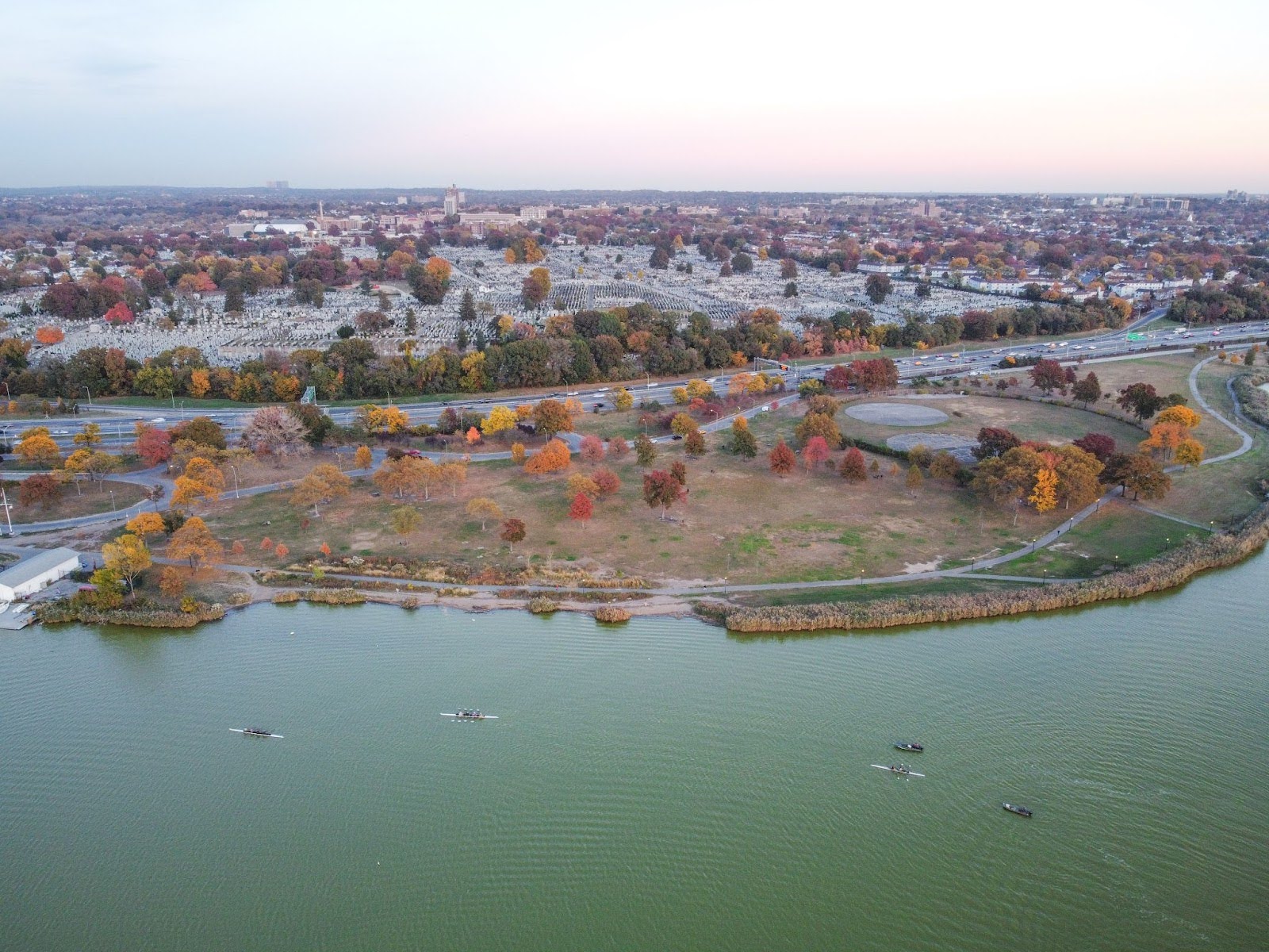 An aerial view of an autumn field next to a river, with city buildings in the background.