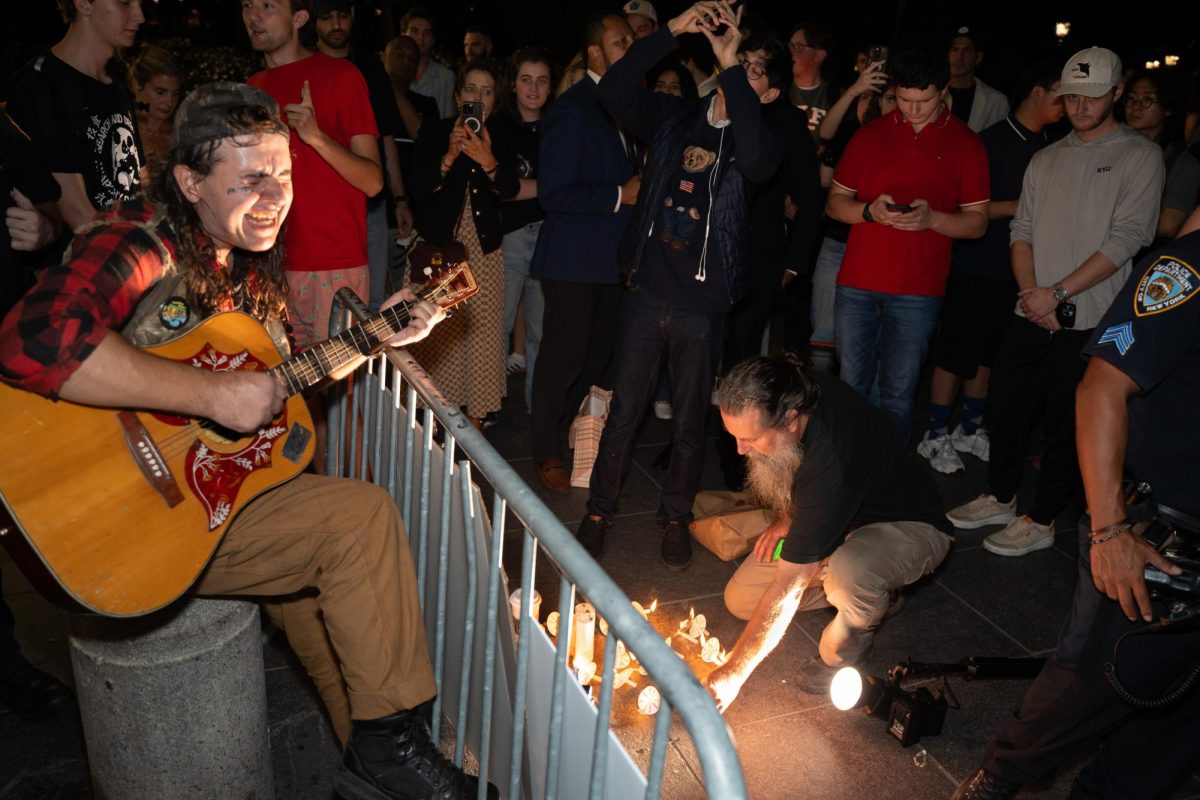 Counter-protestor plays guitar while attendees place candles during a vigil for Charlie Kirk. (Alex Woodworth for WSN)